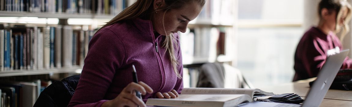 Female student in a pink hoodie studying at a desk in a library