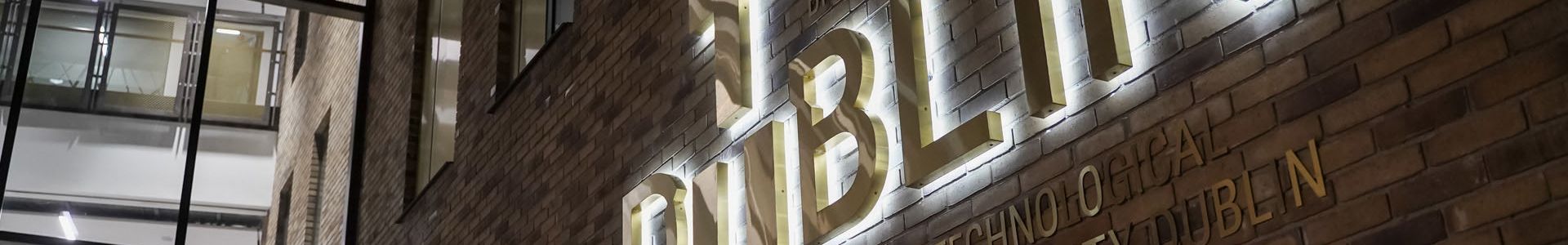 Backlit brass TU Dublin logo at the entrance to the East Quad