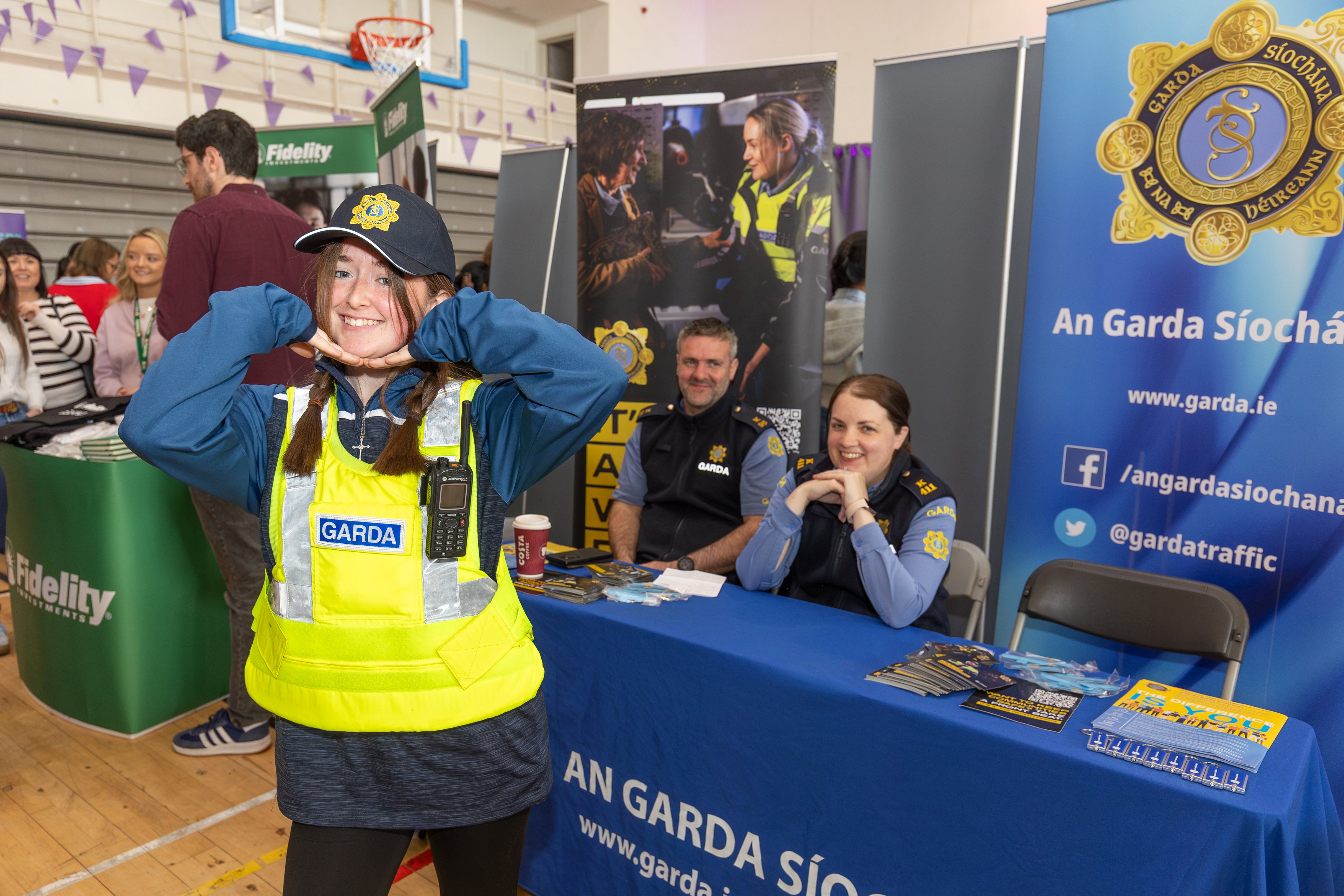 A young participant enthusiastically engages with the exhibition, wearing a bright yellow high-visibility safety vest and a dark cap.