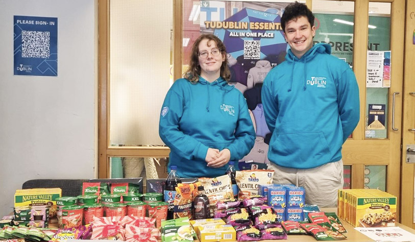 young woman and man in blue college hoodies standing behind a table of pantry food