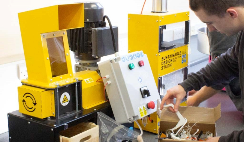 male sifts through a box of items beside a yellow machine which says sustainable design studio