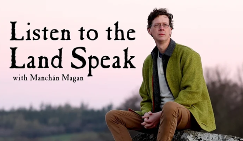 Manchán Magan sits on rock looks out into the distance against rural background with pinkish sky