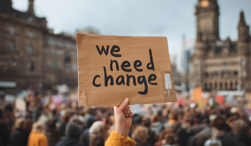Group of people at a protest with sign saying we need change