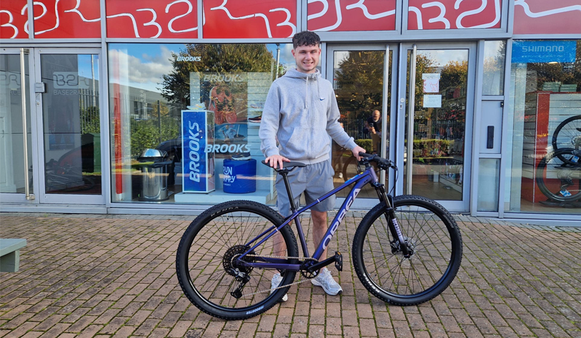 male student standing outside bike shop with new bike