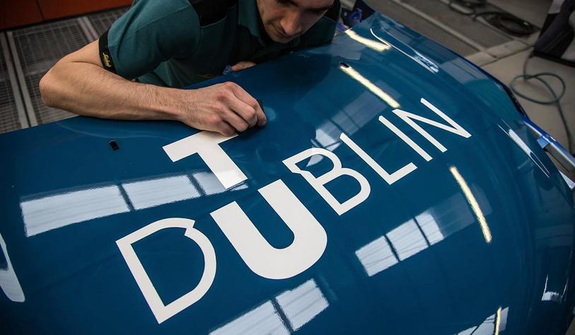 Apprentice working a car bonnet with a TU Dublin Logo