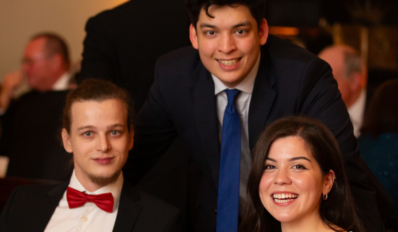 A group of three smiling students at a formal ball wearing black tie
