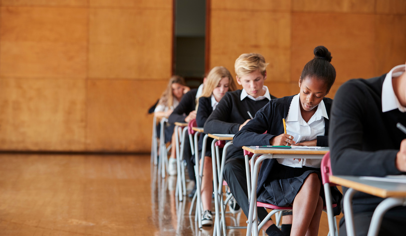 Teenage Students In Uniform Sitting Examination In School Hall