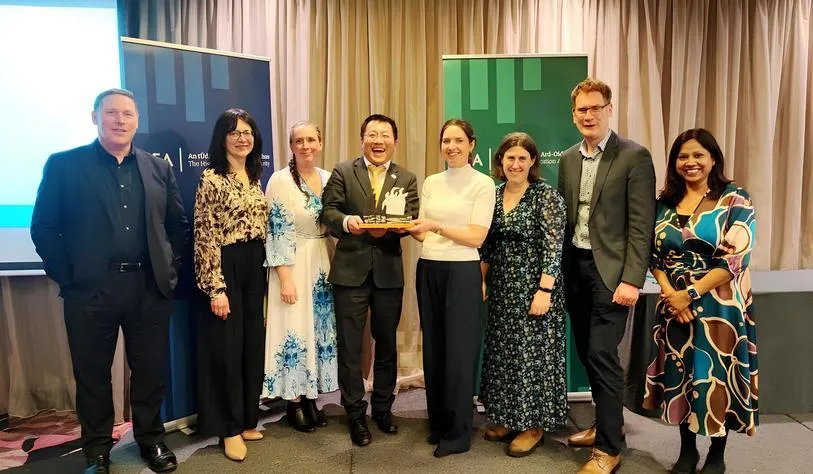 A group of people smile for a photo while one person in the centre holds a trophy