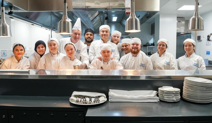 An image of a large group of chefs standing at the pass between the kitchen and restaurant floor