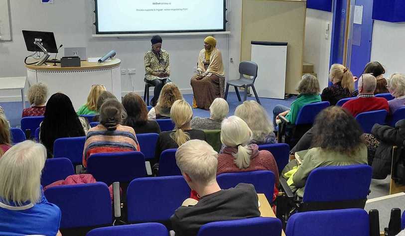 A group of people in a tiered lecture hall listen to a panel of speakers