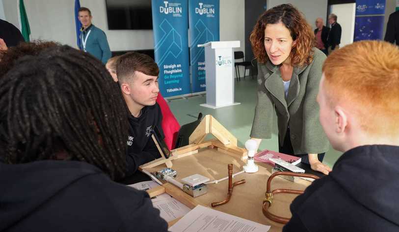 A person talking to three people at a table with electrical equipment