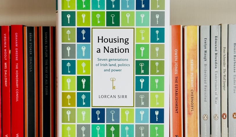 A bookshelf featuring Housing a Nation: Seven Generations of Irish Land, Politics and Power by Lorcan Sirr at the center, with a colorful key-pattern cover.
