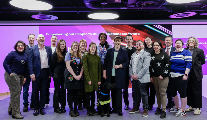A large group of people smiling happily, there is a black dog in the centre.