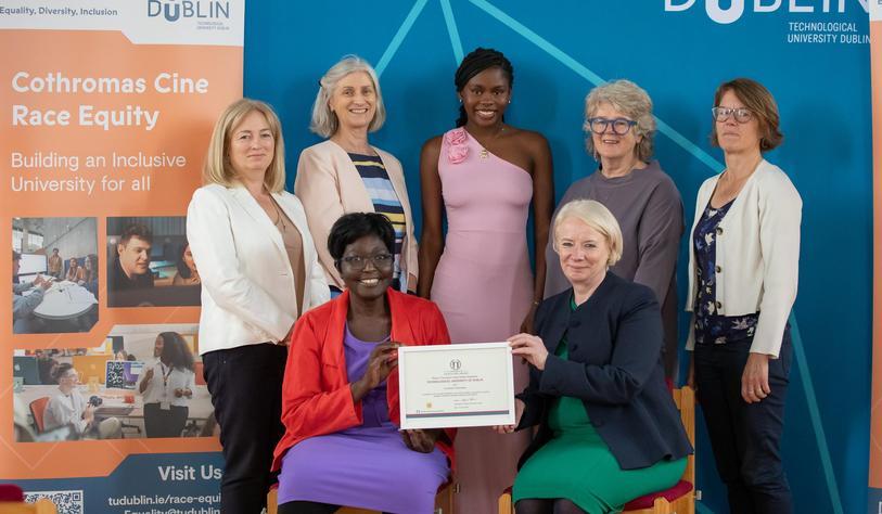 A group of people post with a certificate in front of a blue banner