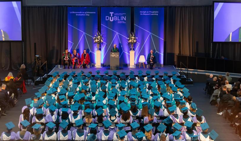 Overview of the Technological University Dublin graduation ceremony, with rows of graduates in turquoise and blue academic gowns seated in front of the stage.