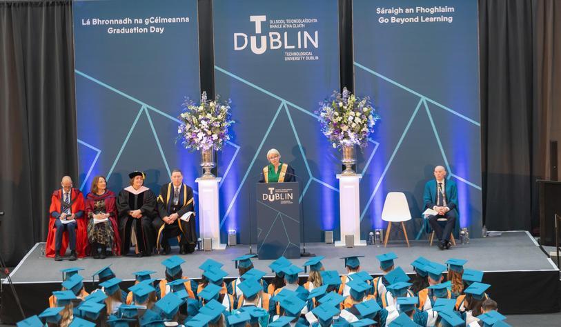 An image of people attending a Graduation Ceremony in a hall with robes in Blue and Green