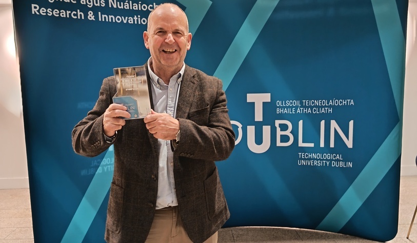Image of Dr Keith Muprhy holding an award in front of a banner of the TU Dublin logo