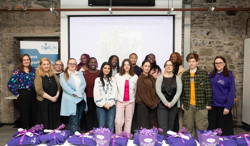 A group of people pose in front of a screen with Happy International Women's Day