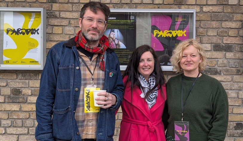 A group of people pose in front a brick wall with posters that have text saying Paradox
