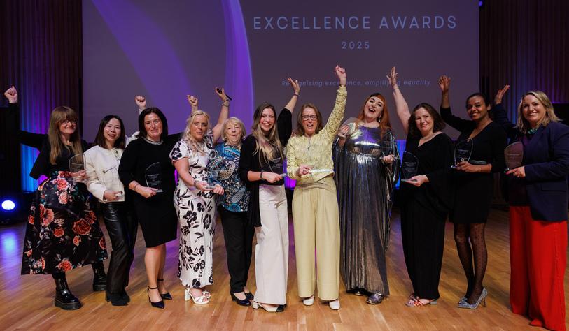 A group of women and awards winners standing in front of a banner with their hands in the air