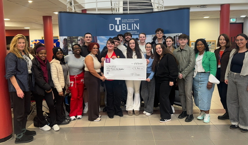 A group of students standing in front of a TU Dublin stand holding a large cheque
