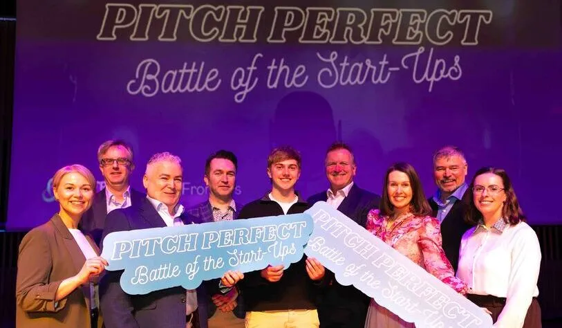 A group of nine people stand smiling on stage, holding signs that read, 