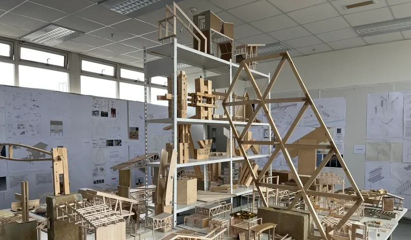 Architectural studio with wooden models and sketches displayed on walls. The models vary in size and complexity, conveying creativity and innovation.